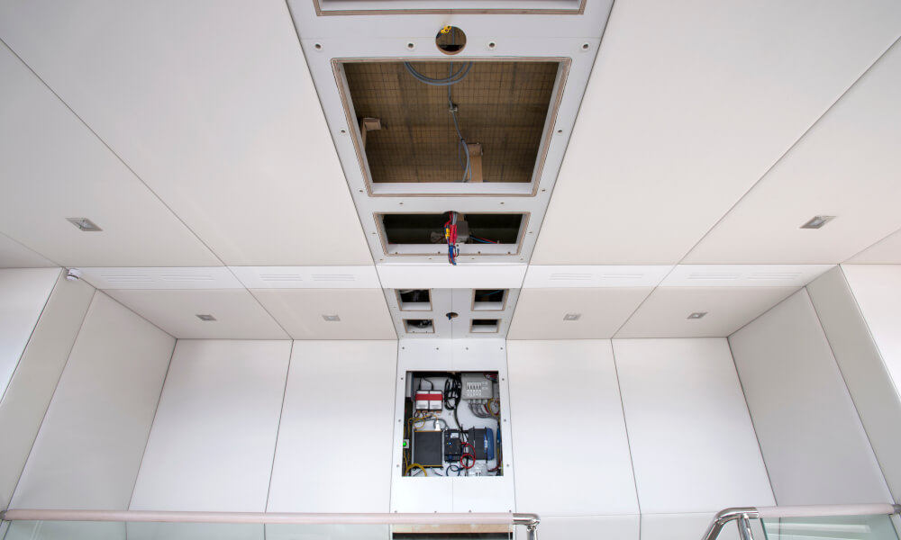 Access panels - after Interior space showing a white ceiling with recessed lighting and a rectangular opening, alongside exposed wiring and components in the wall during construction, related to marine panel fasteners.
