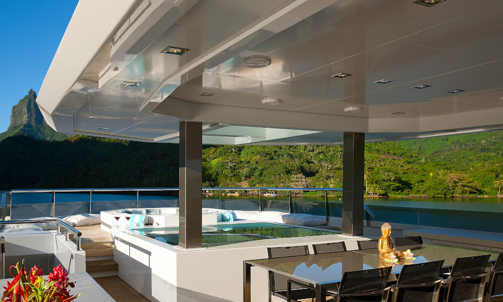 Deckheads - after Luxury yacht deck with Jacuzzi and outdoor dining area overlooking tranquil waters and mountains, highlighting premium marine craftsmanship using marine panel fasteners.